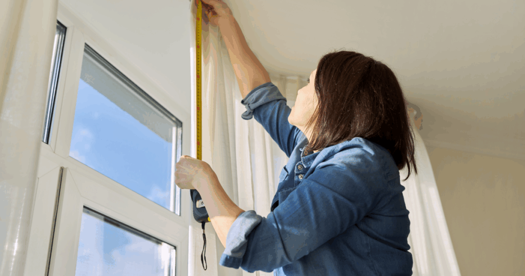 Woman measuring a window frame with a tape measure for custom blinds installation in a bright home.